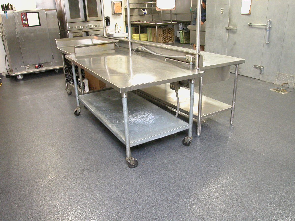 Blue-gray flake epoxy floor around a long stainless prep table in a commercial kitchen