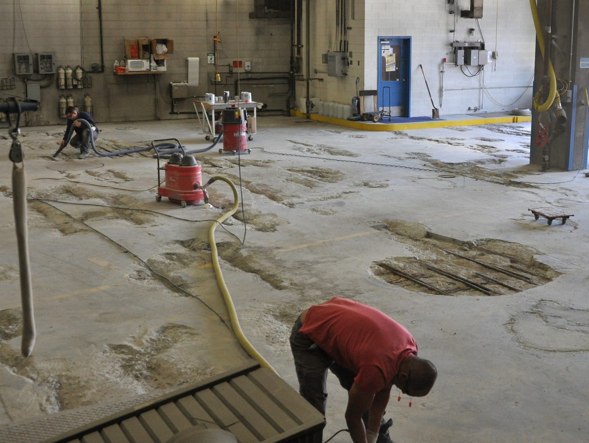 Failed concrete being ground and vacuumed in a road maintenance shop before coating