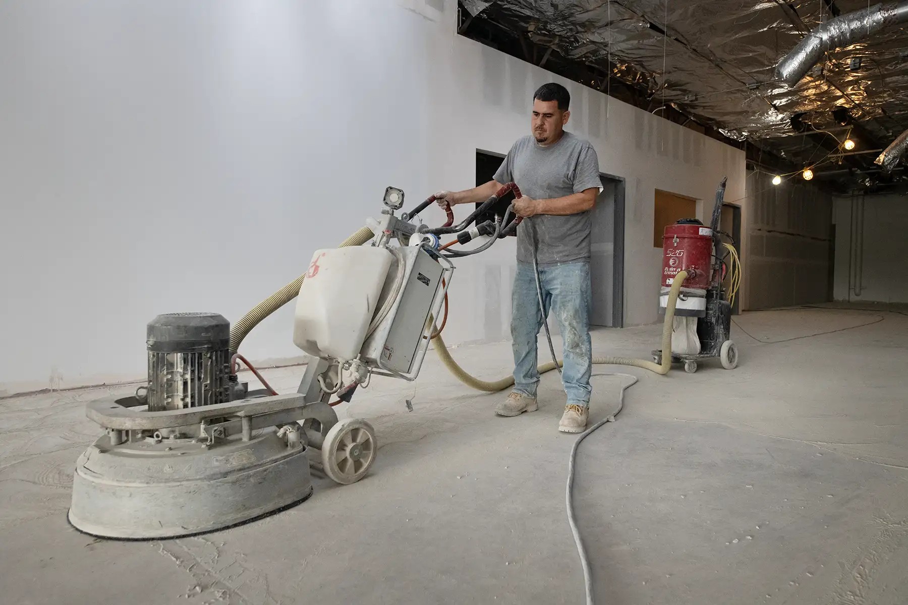 A Western Concrete Coatings crew member grinding a concrete floor with a planetary grinder and dust extractor