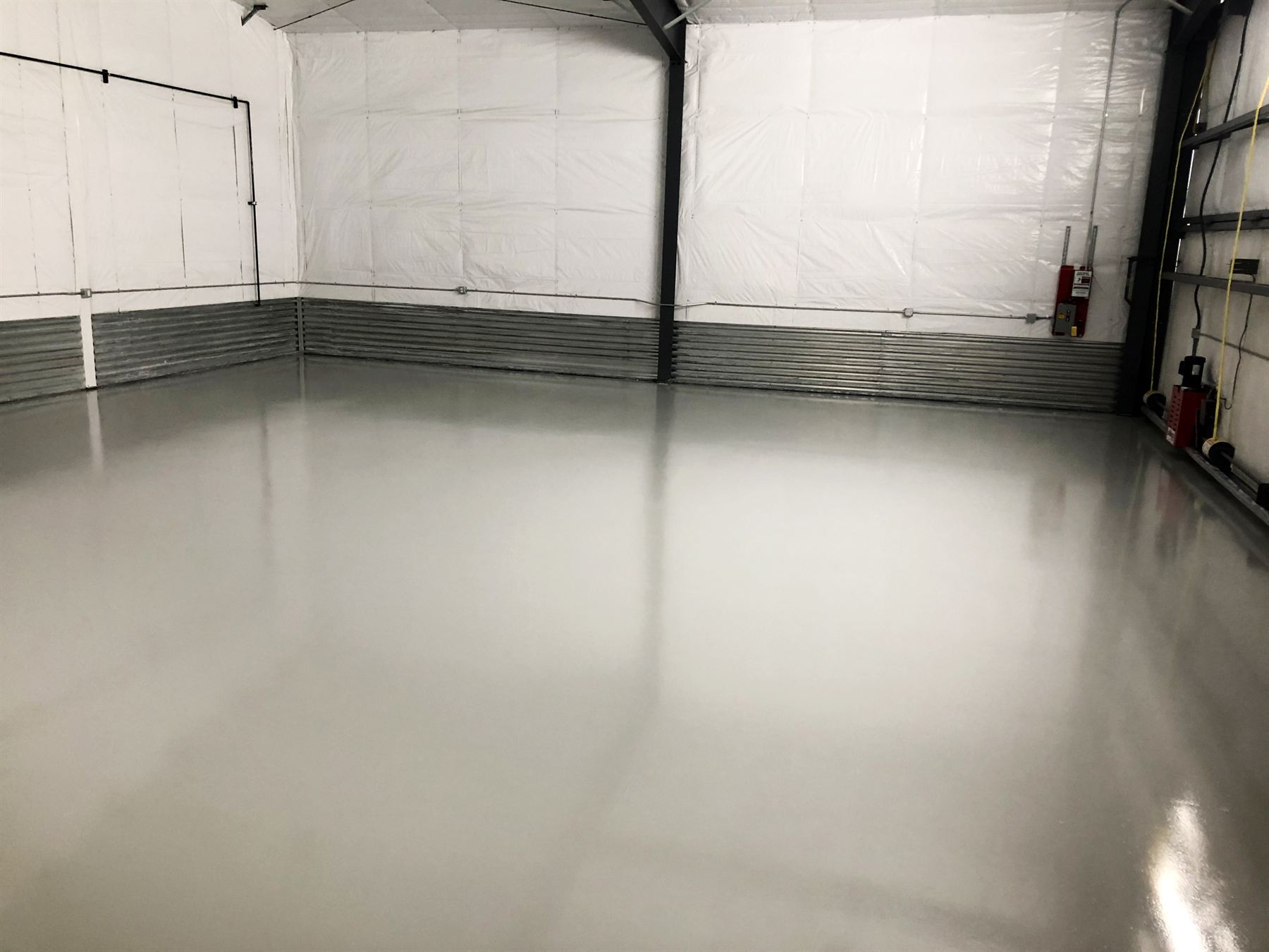 Glossy light gray epoxy floor in an empty commercial hangar with white walls