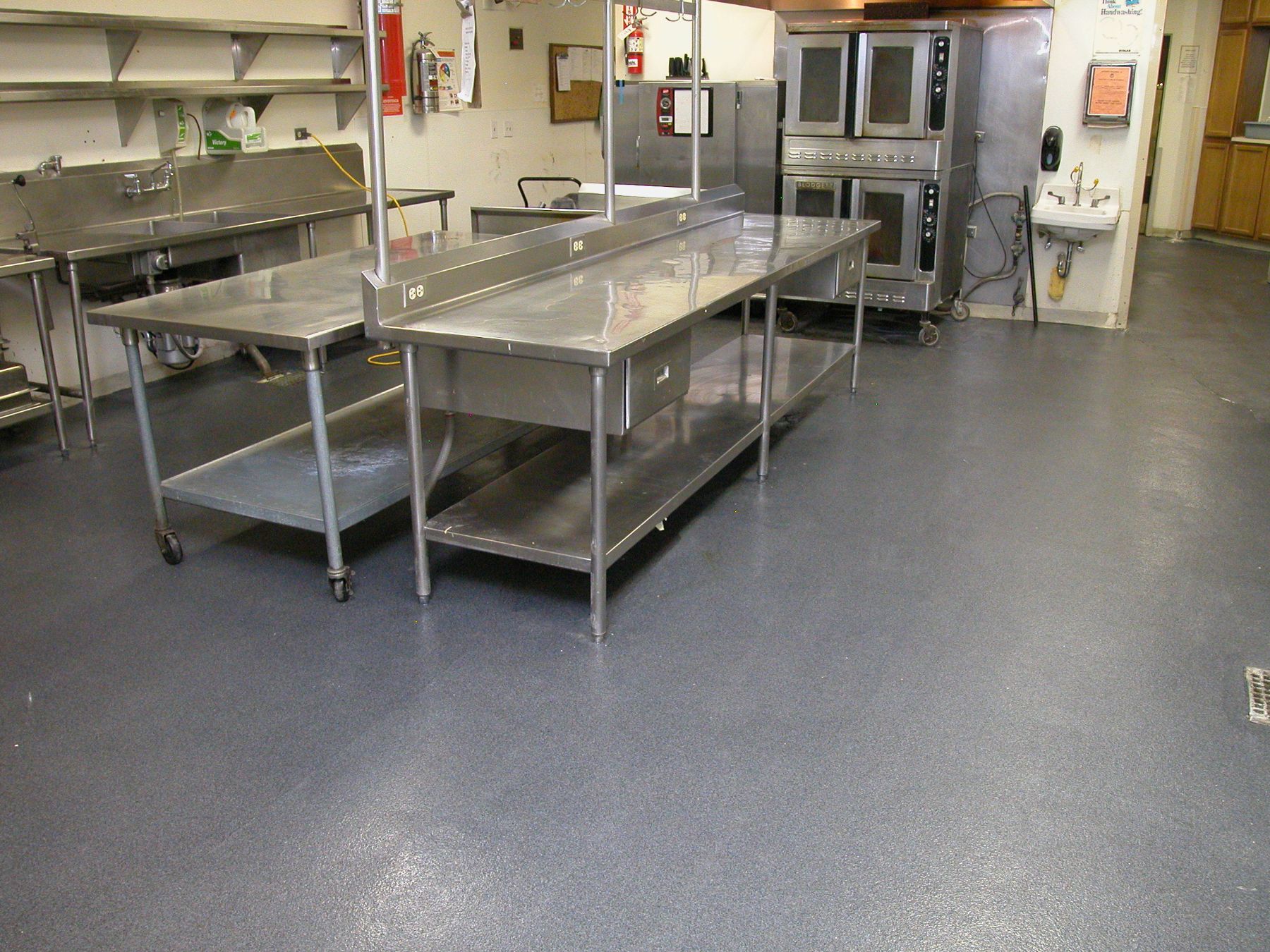 Gray speckled epoxy floor in a commercial kitchen with stainless steel prep tables and convection ovens