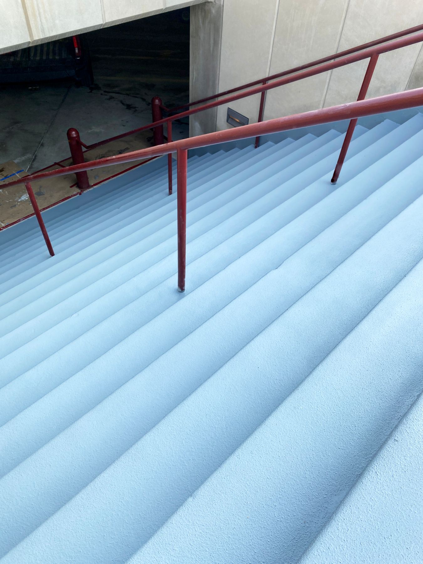 Long concrete staircase coated in light gray textured non-slip coating with red metal handrails