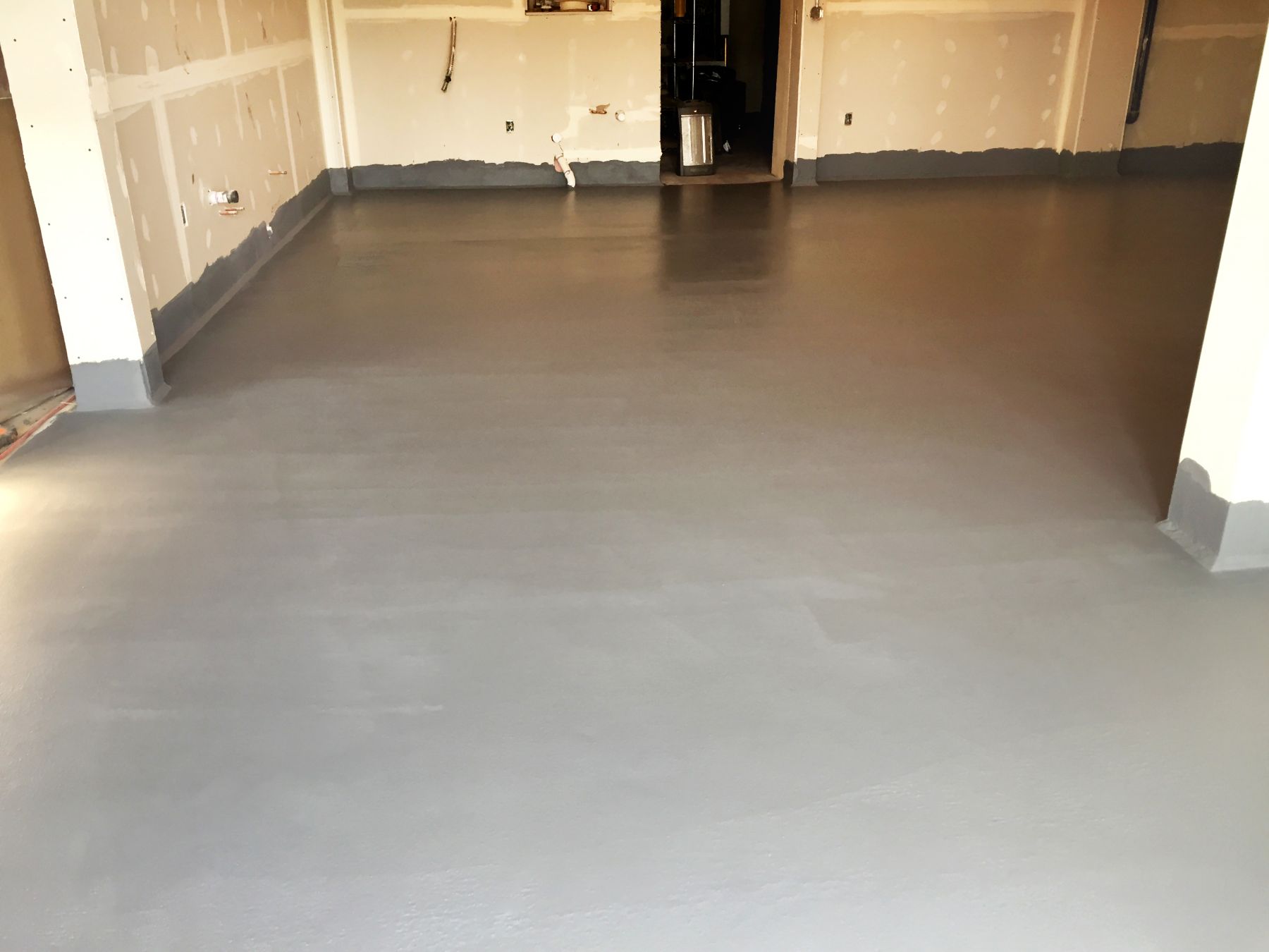 Freshly coated smooth gray concrete floor in an unfinished room with bare drywall walls