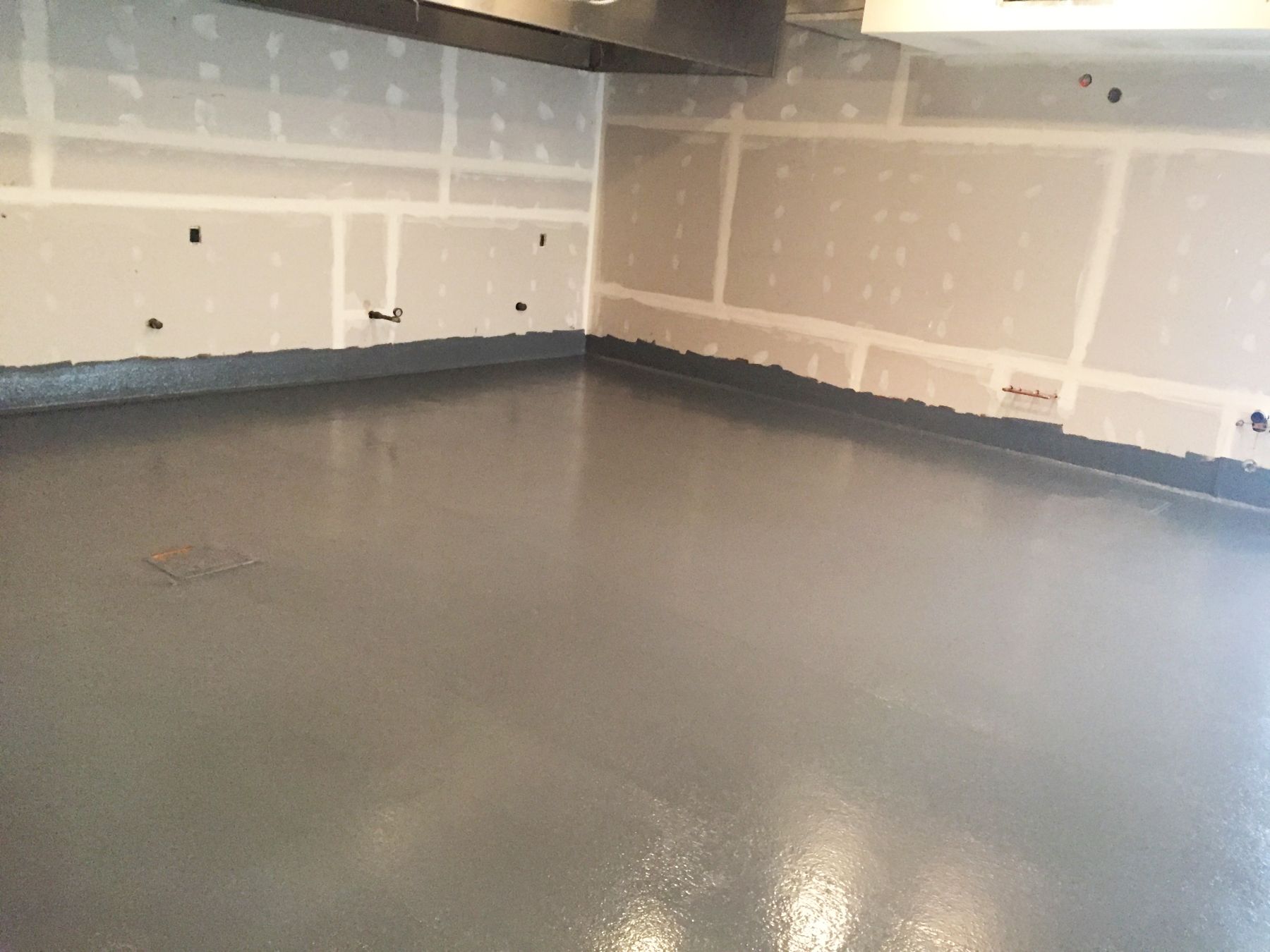 Glossy gray speckled coated floor in a commercial kitchen under construction with unfinished drywall walls