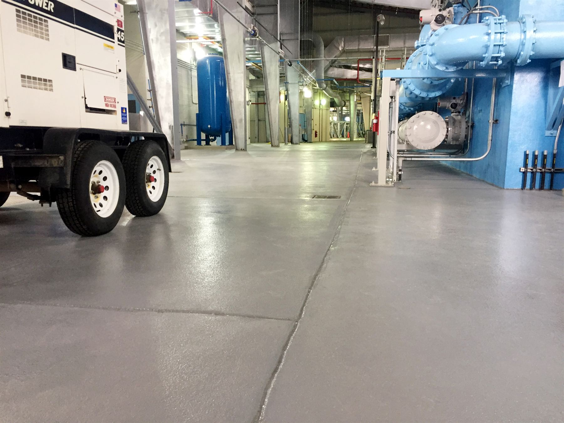 Gray textured concrete coating with sealed joints in an industrial pump room with blue piping