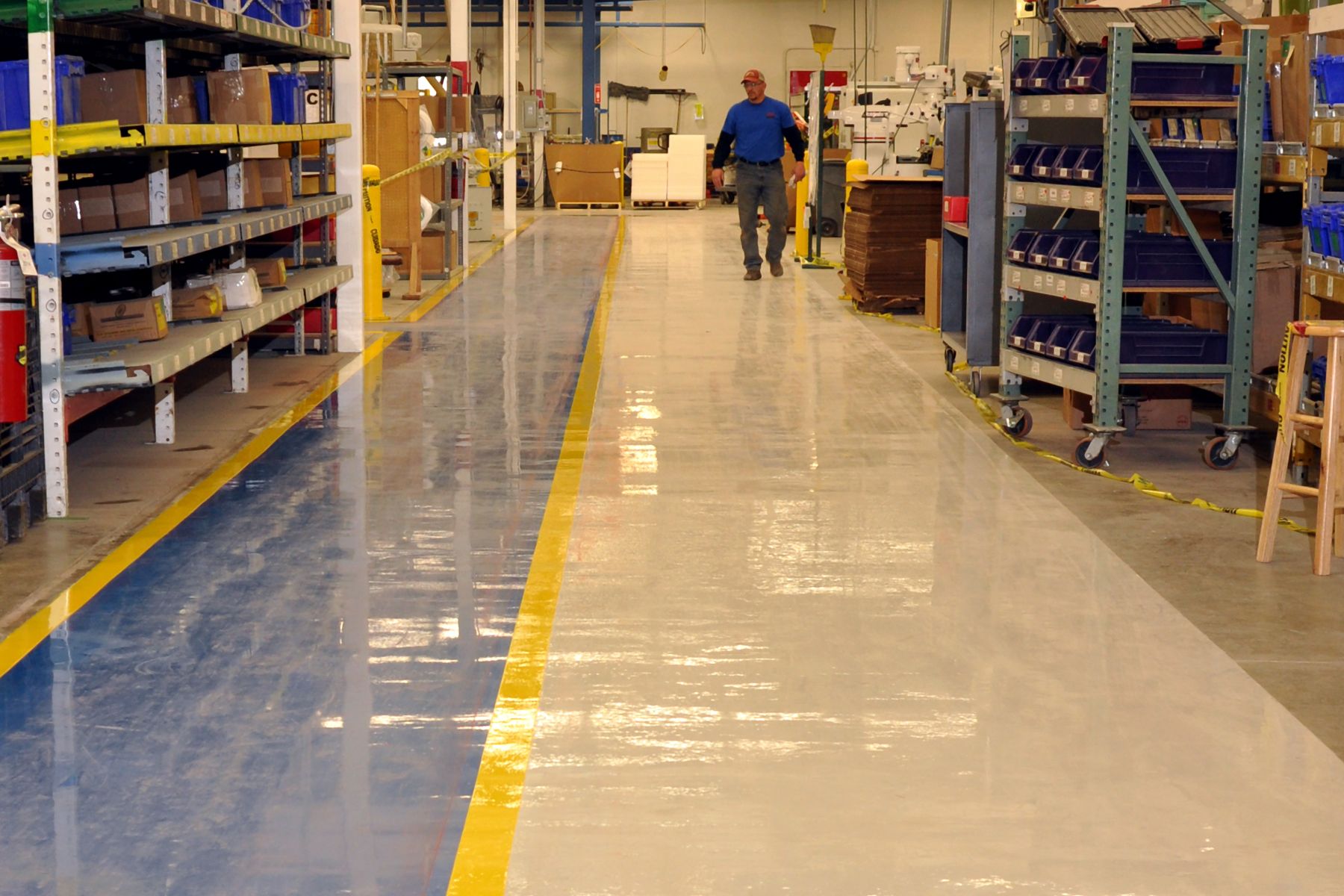 Glossy epoxy warehouse floor with blue and beige sections separated by yellow safety stripe between shelving