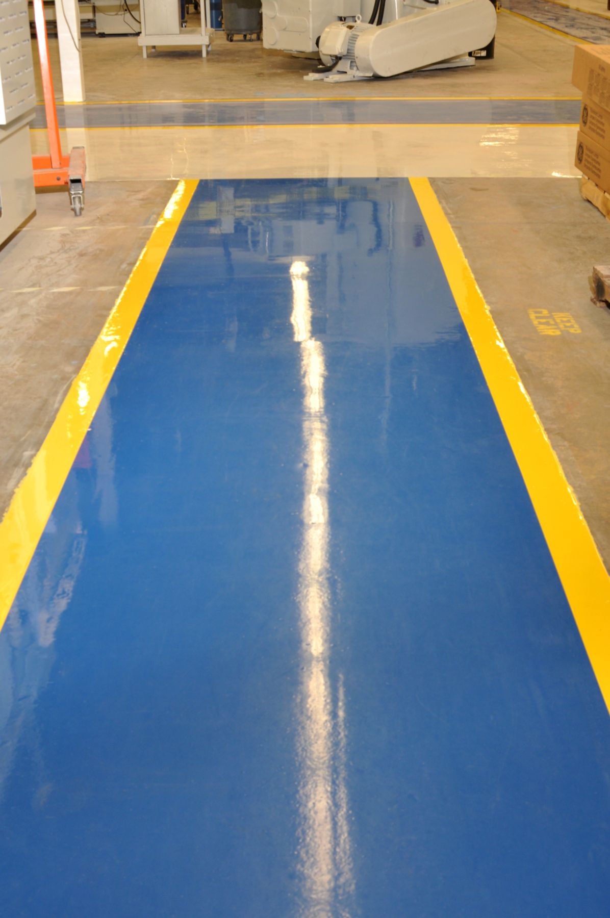 Glossy blue epoxy walkway with yellow safety borders running through a manufacturing facility floor