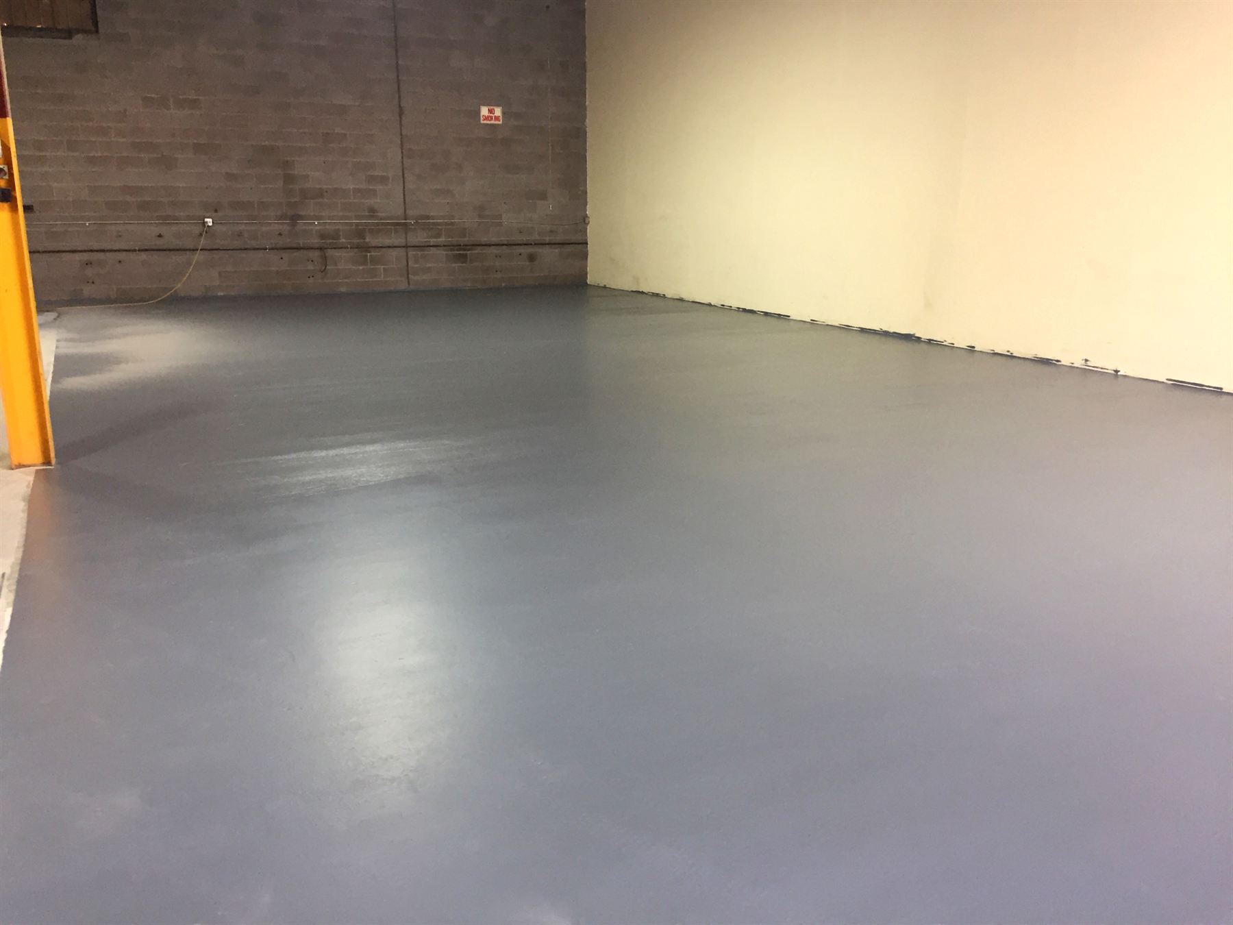 Smooth gray epoxy-coated warehouse floor beside cinder block wall and cream wall
