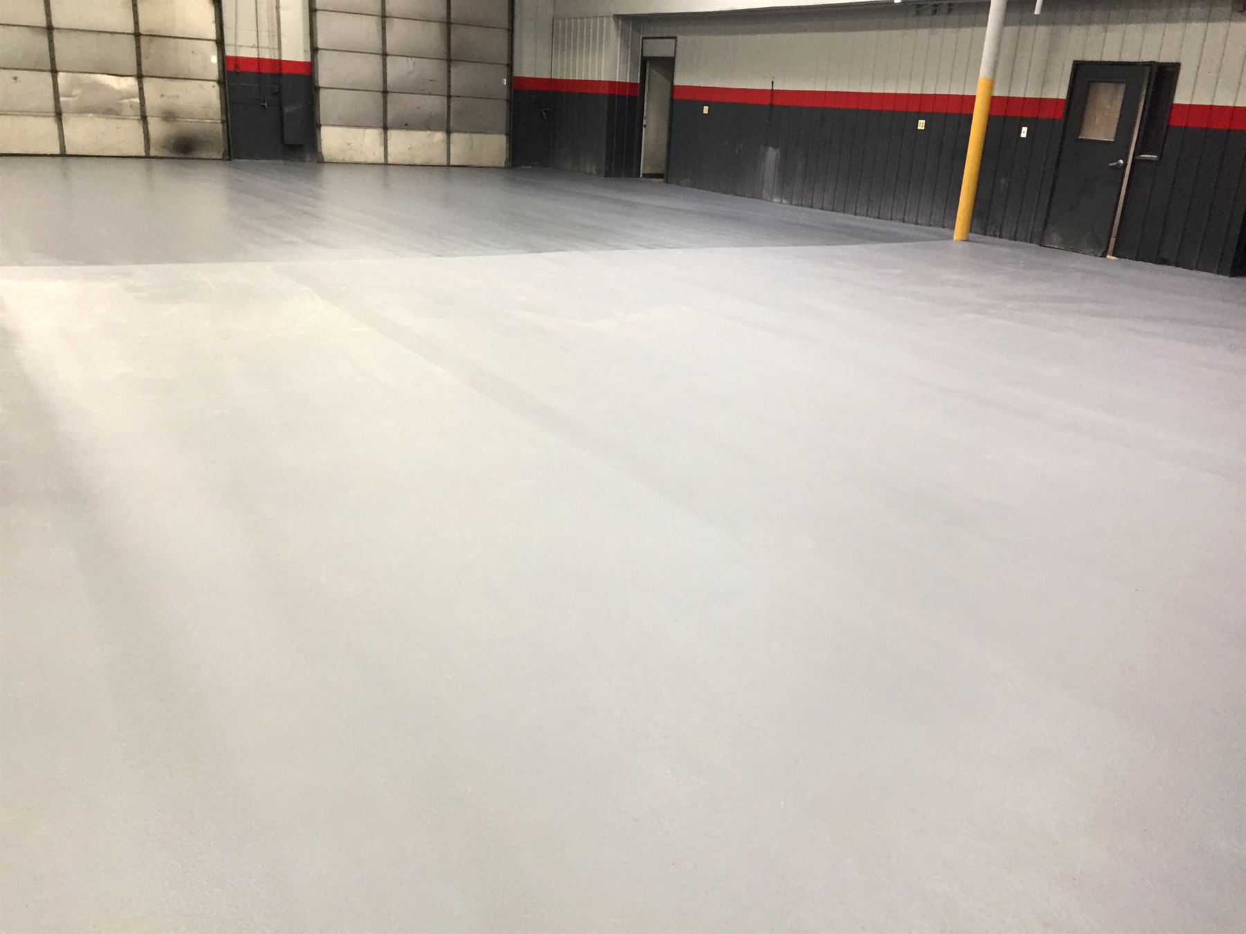 Light gray epoxy-coated shop floor in a large garage bay with red-striped walls