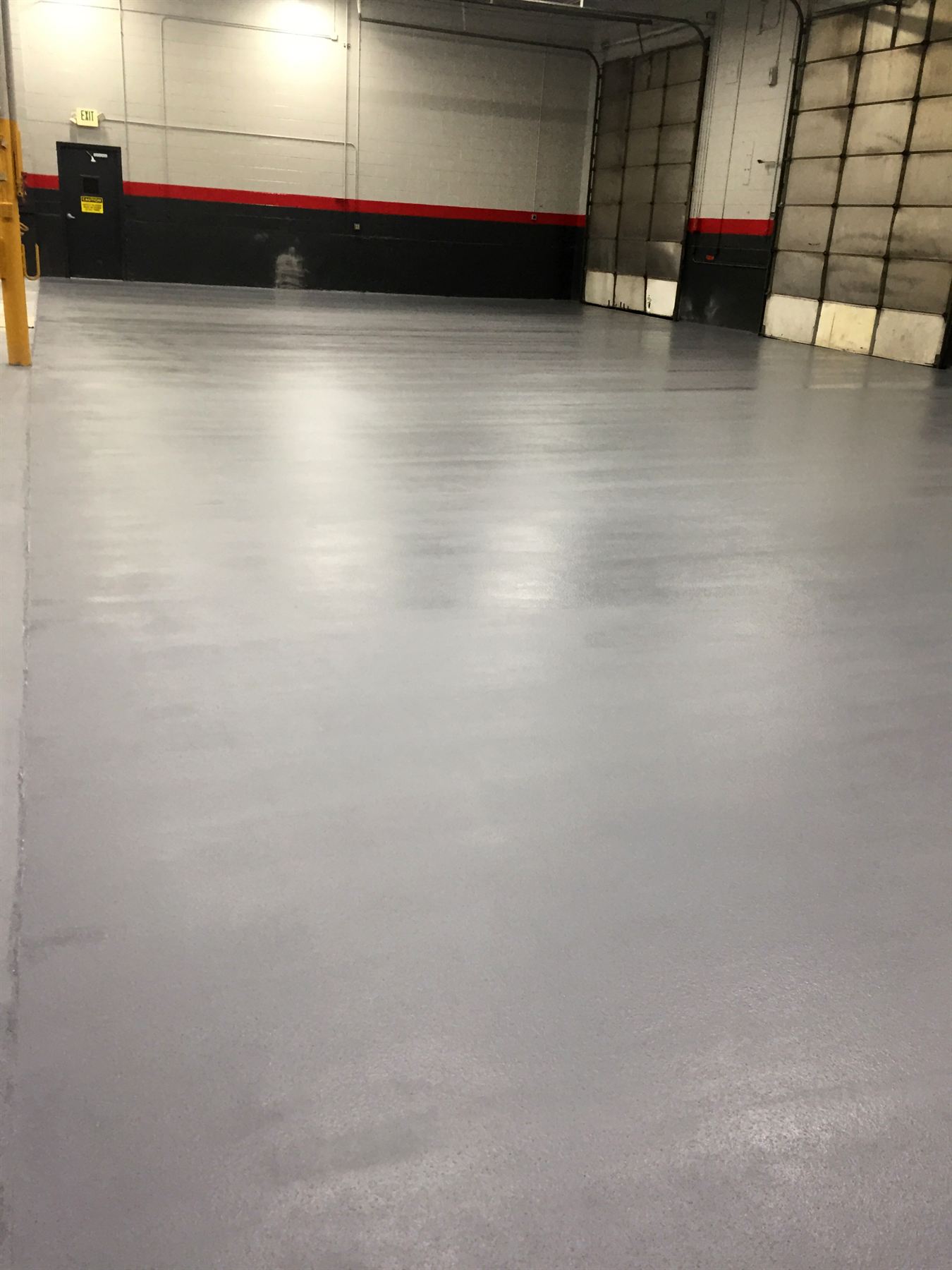 Glossy gray epoxy warehouse floor with red-striped black walls and loading dock doors