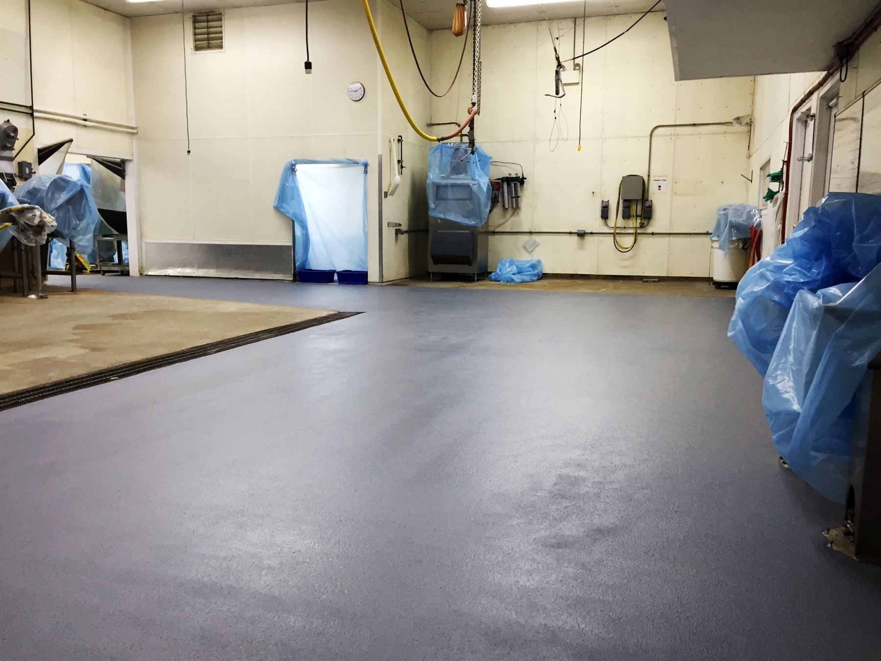 Blue-gray epoxy floor in a food processing room, bare stained concrete section beside drain