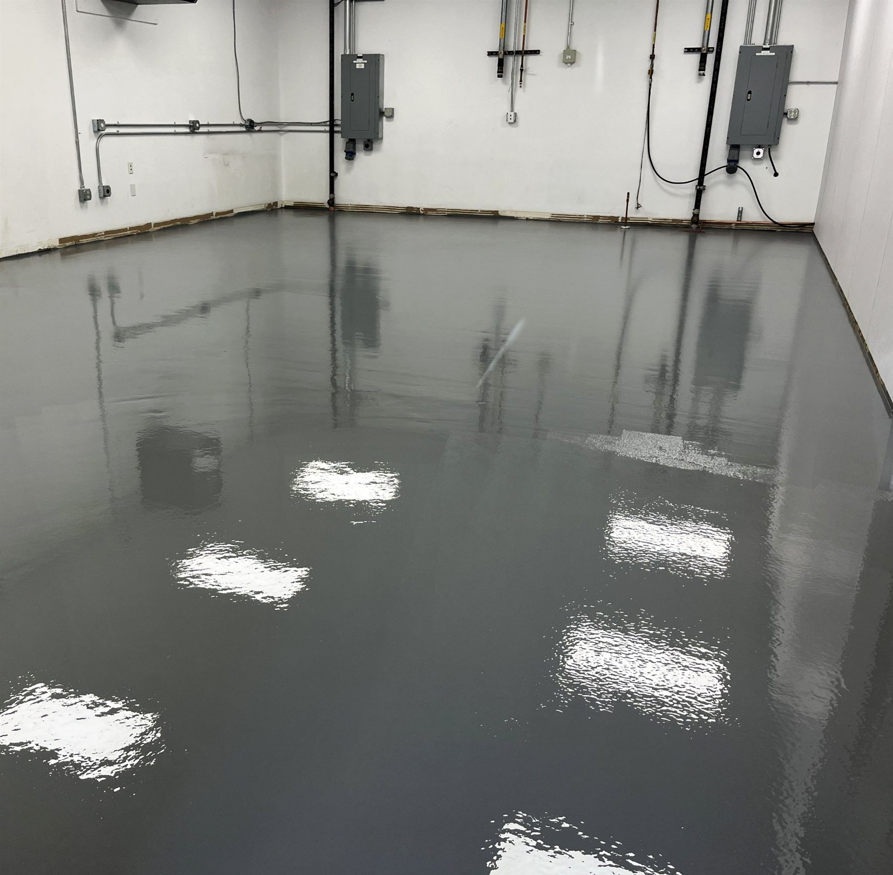 Glossy dark gray ESD epoxy floor in a white-walled electrical equipment room with panels and conduit