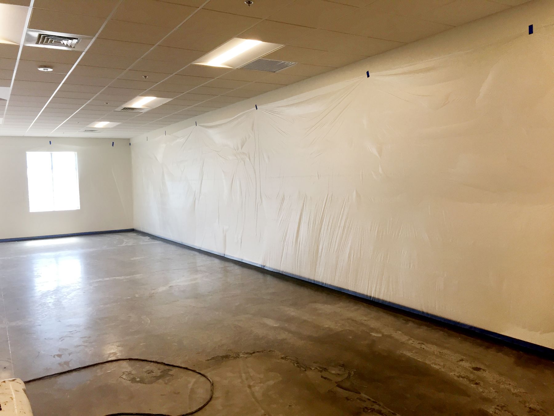 Bare ground concrete floor in an empty room with walls masked in plastic and blue tape