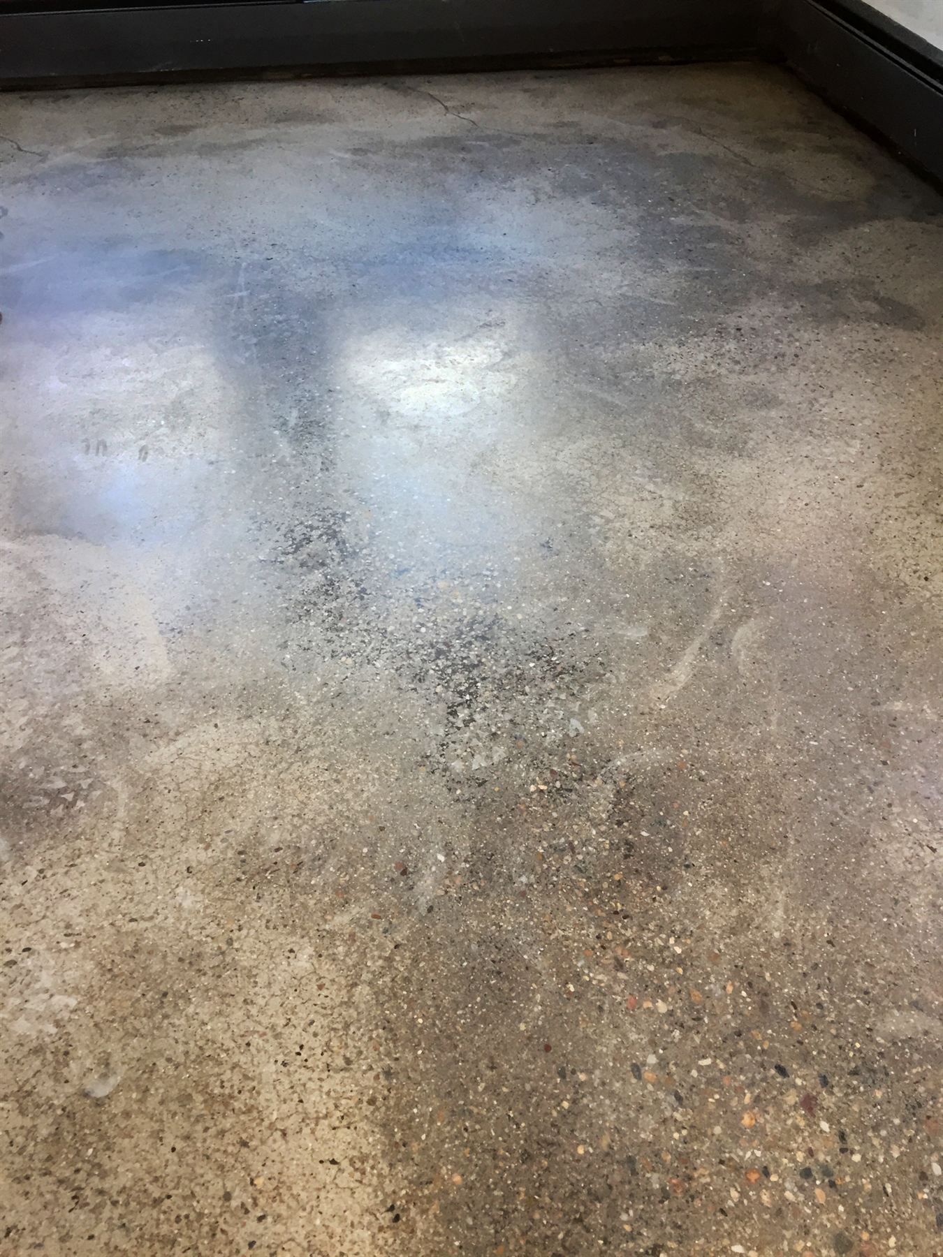 Close view of mottled gray and tan concrete floor with swirl marks and patchy, uneven sheen