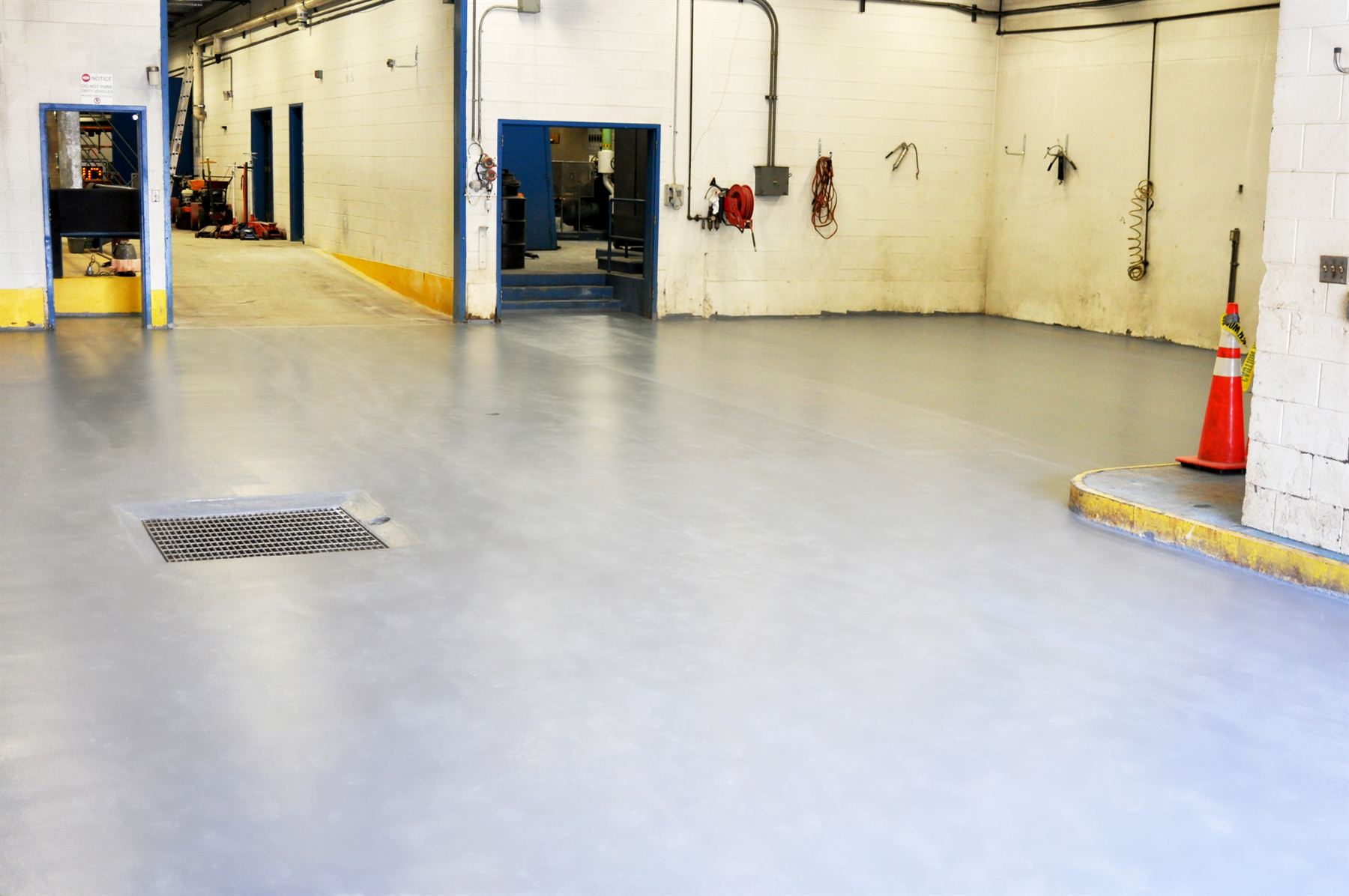 Light gray coated concrete floor with a metal drain grate in an industrial maintenance bay