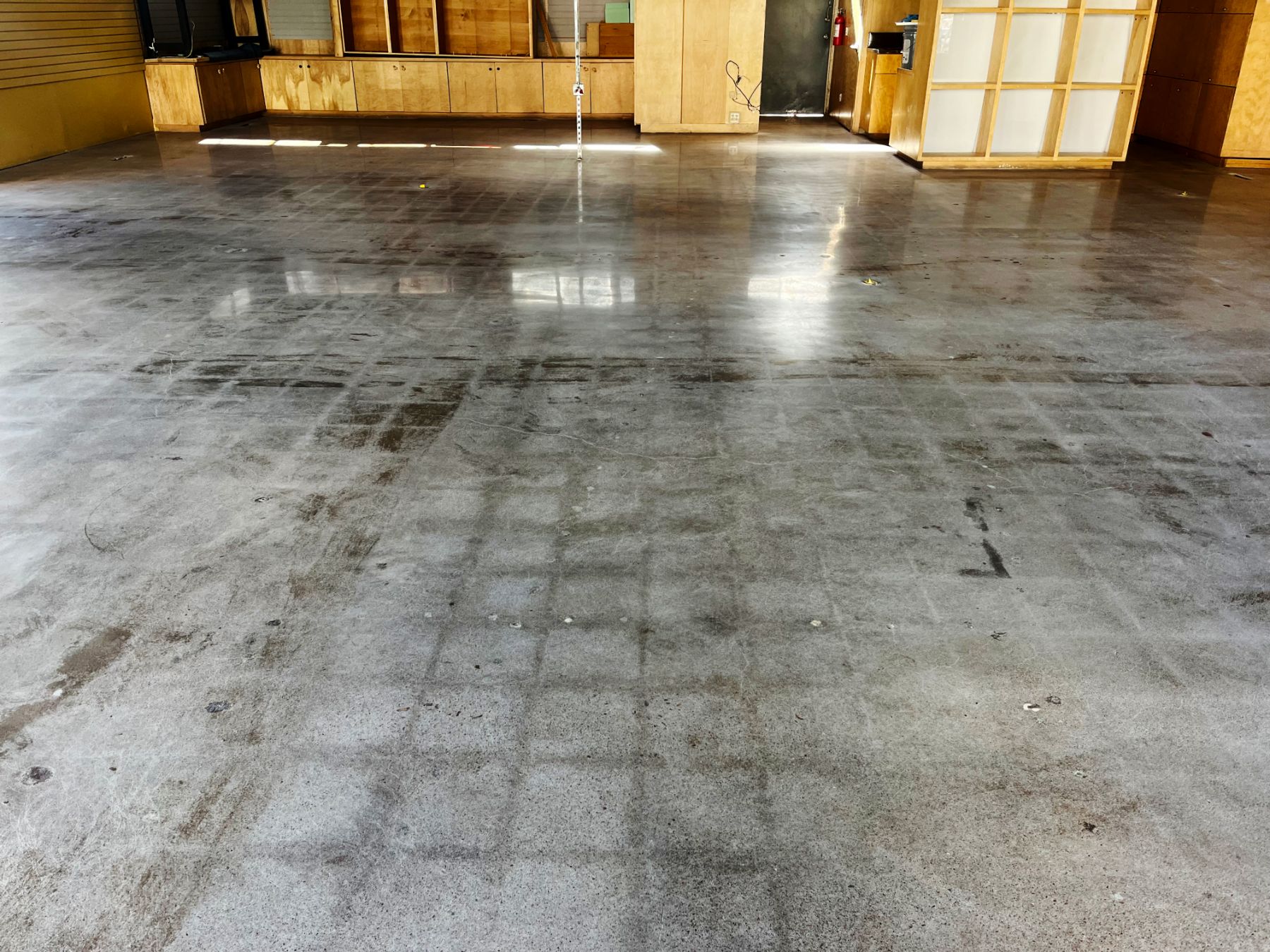 Stained polished concrete floor with tile-grid ghosting in an empty retail space with wood cabinetry