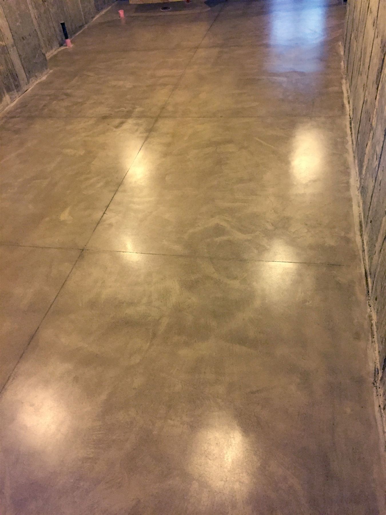 Glossy polished concrete floor with a soft mottled finish and saw cut joints in a long narrow room