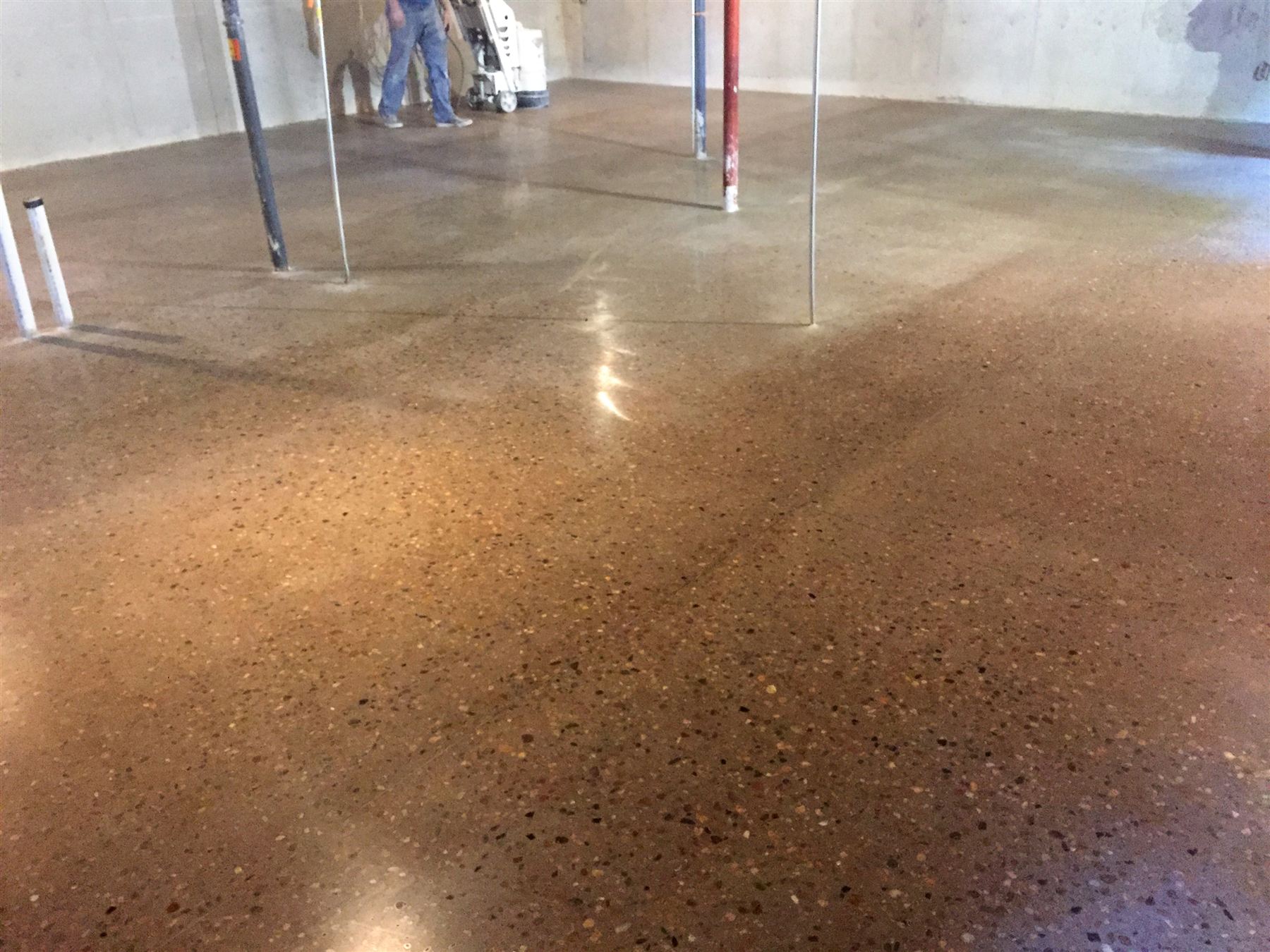 Polished concrete floor with exposed tan and brown aggregate and a grinder at work in a large open room