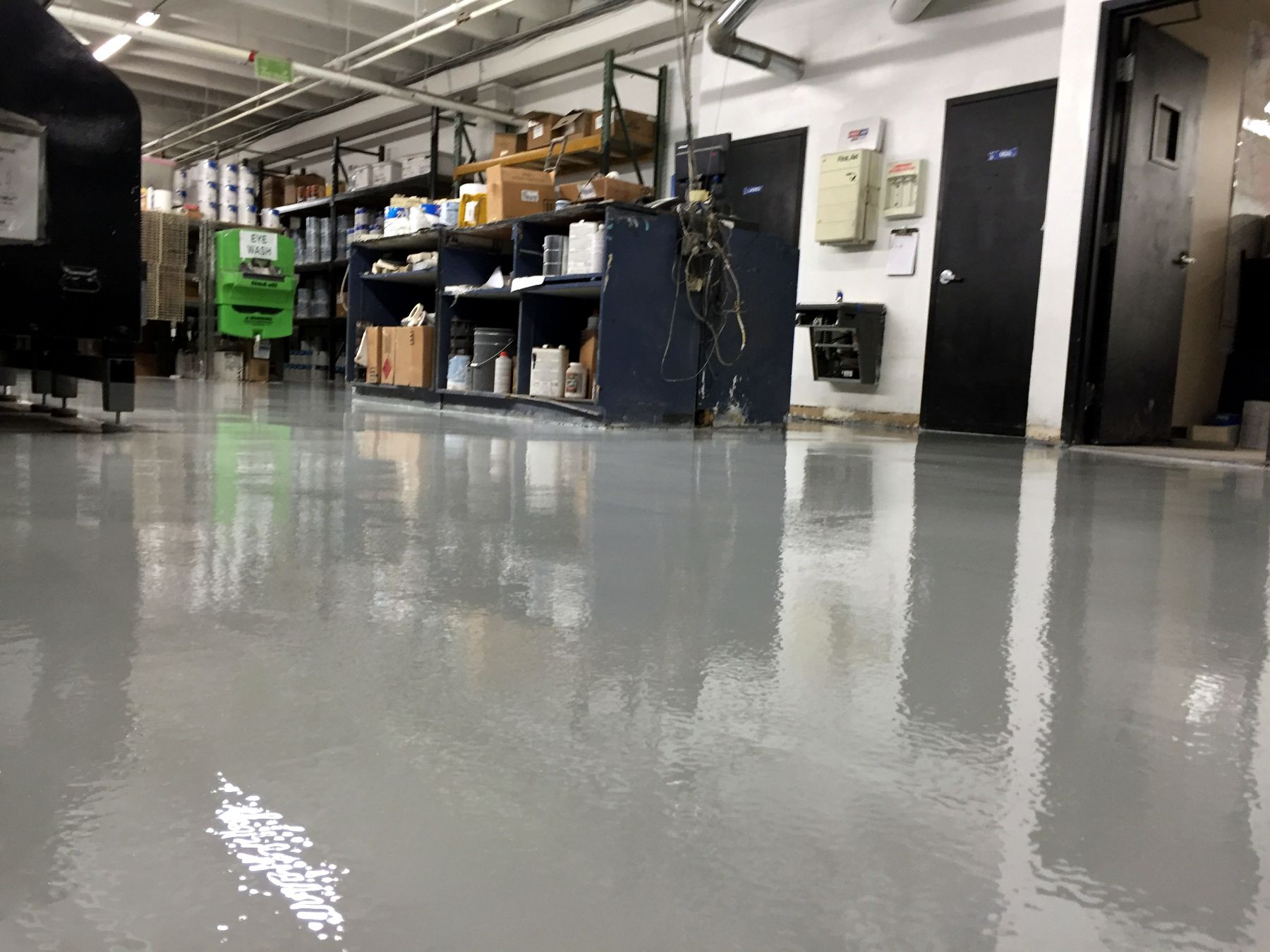 Glossy light gray resinous floor in an industrial workshop with shelving, supplies and black doors