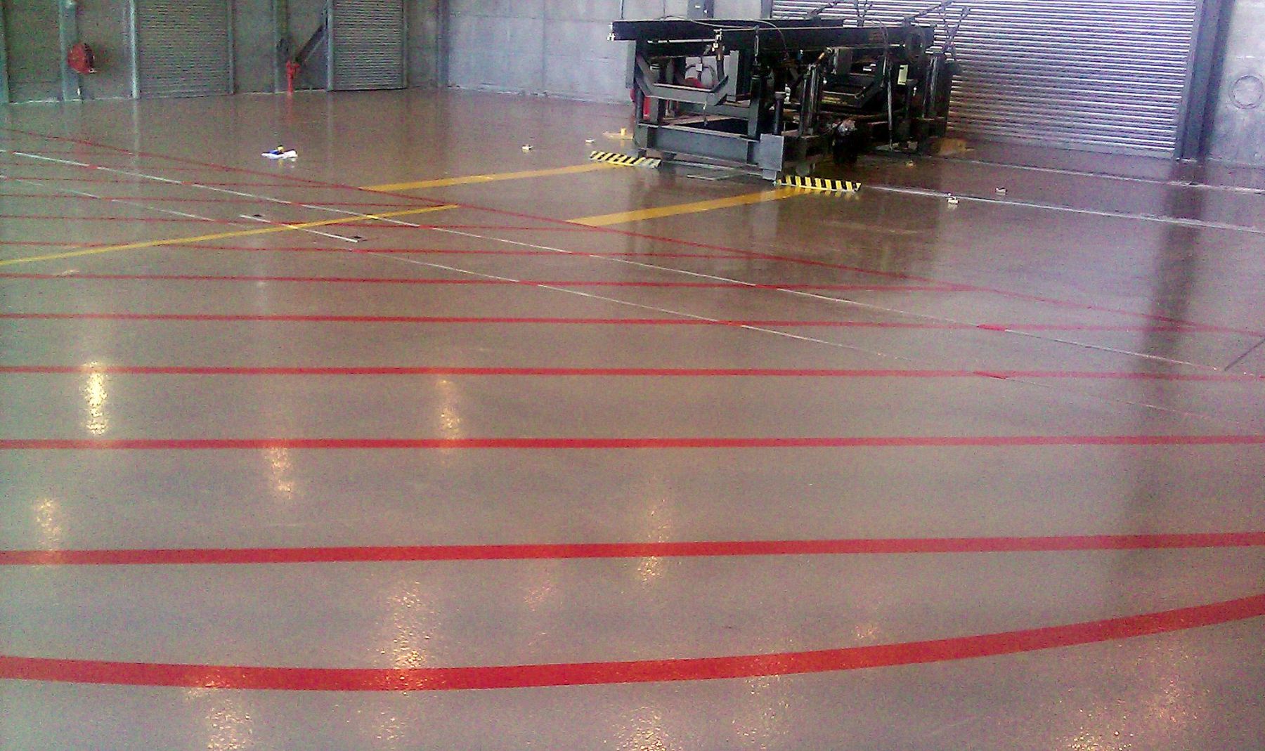 Glossy tan resinous hangar floor with red and yellow safety striping across a large open industrial space