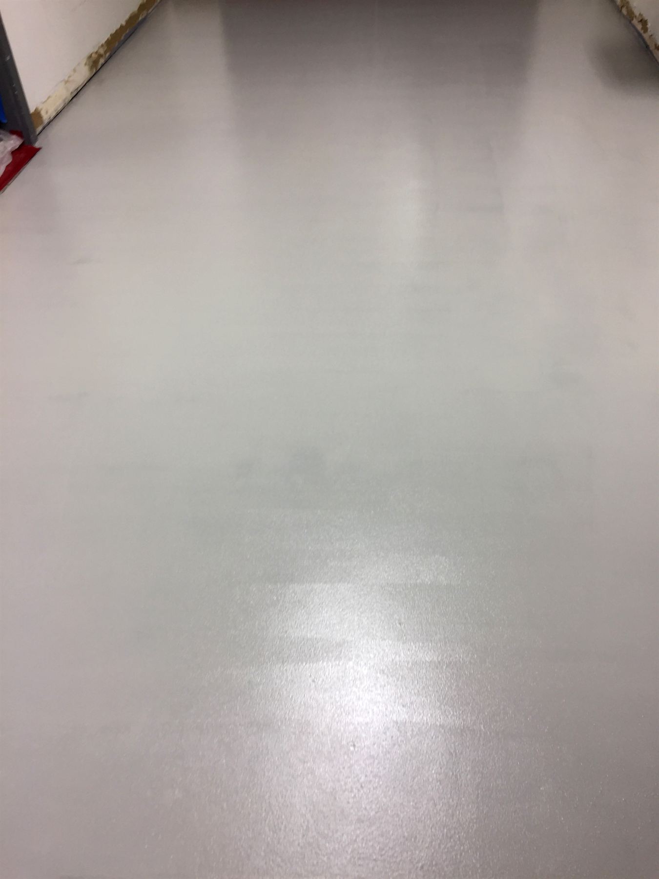 Light gray seamless resinous floor with fine textured finish running along a white wall