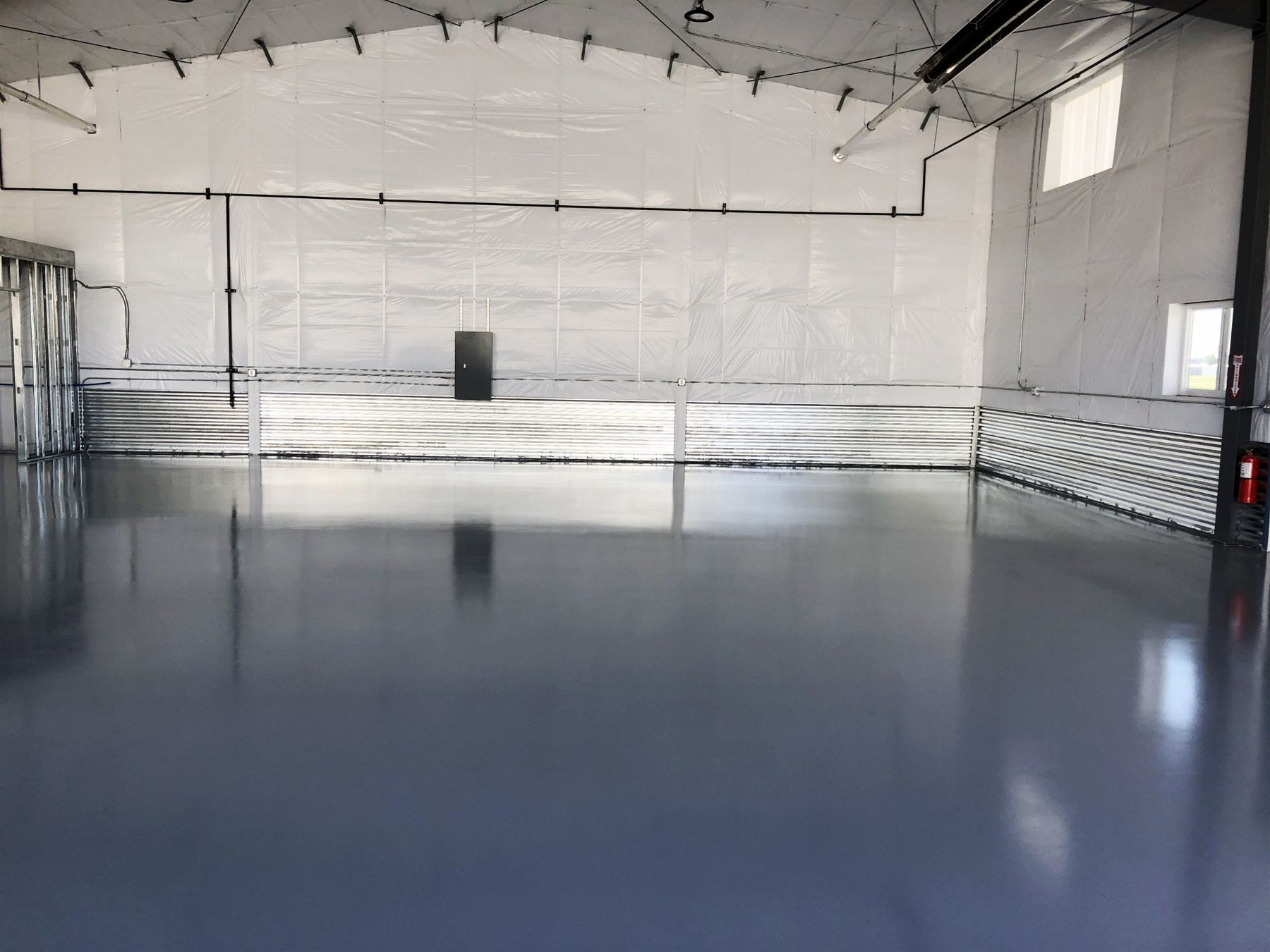 Glossy blue-gray seamless epoxy floor in a large white hangar with corrugated metal wall base