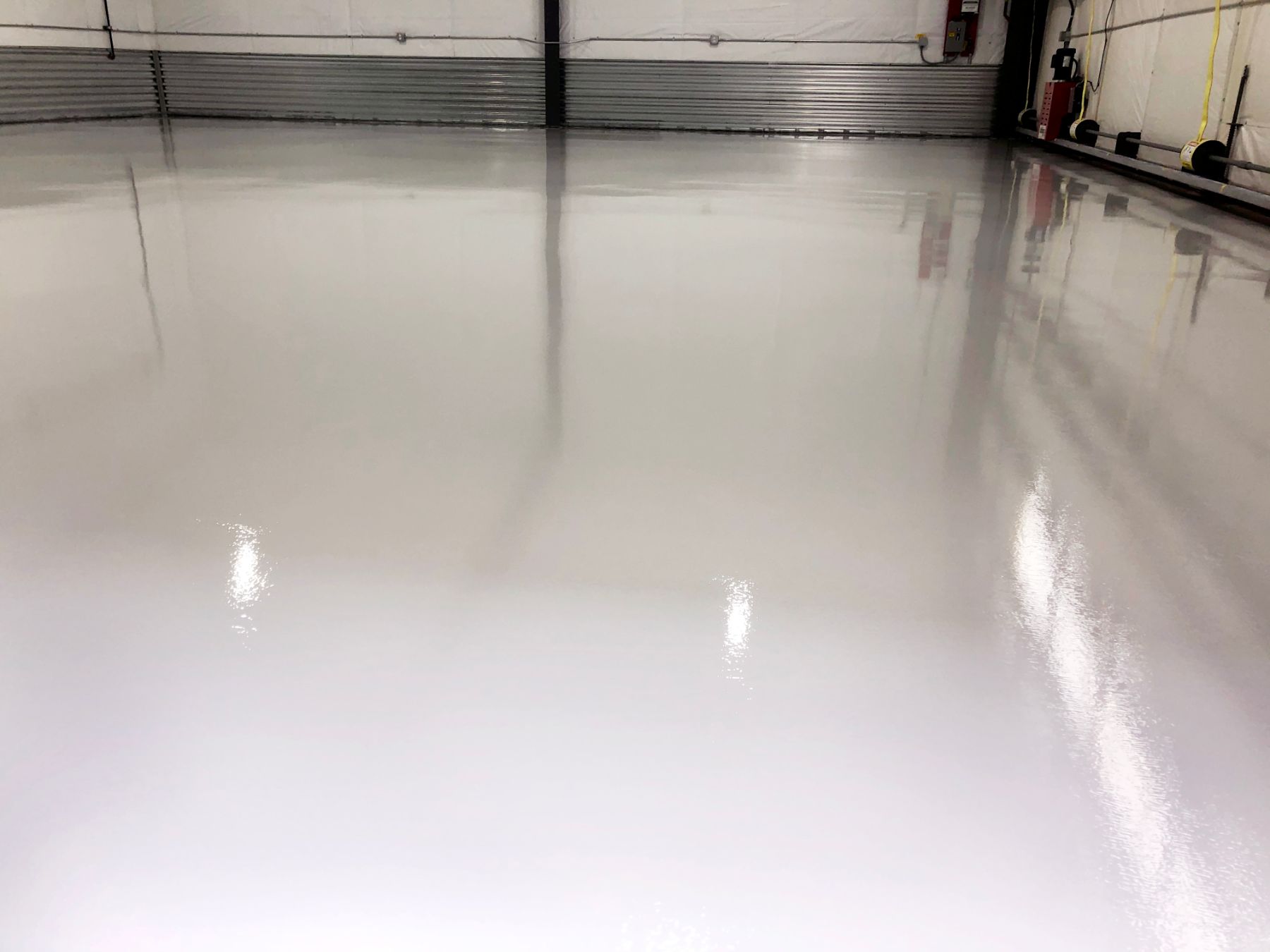 Glossy light gray seamless epoxy floor in an aircraft hangar with reflections of equipment and corrugated metal walls