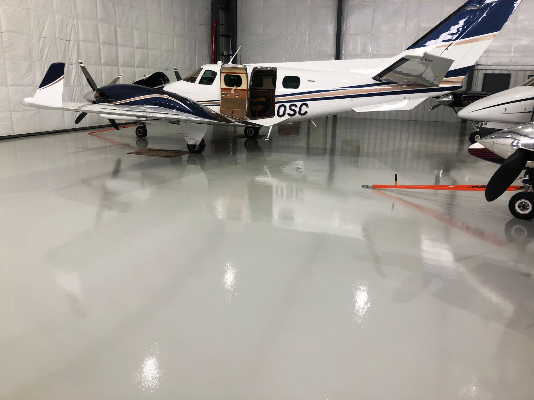 Light gray glossy seamless epoxy hangar floor with a parked twin-engine airplane and orange tow bar