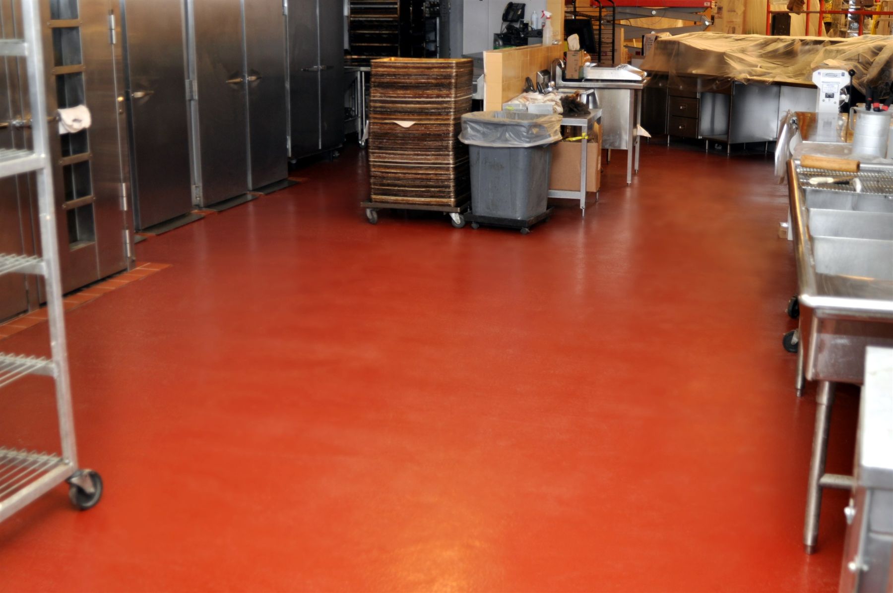 Terracotta red seamless floor in a commercial bakery kitchen with stainless coolers, sinks and stacked baking trays