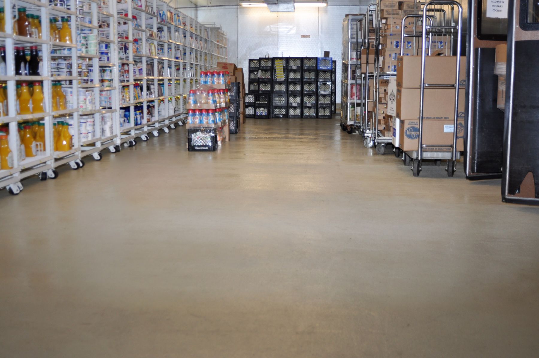 Smooth tan seamless floor in a grocery dairy cooler aisle with shelving, milk crates and loaded carts