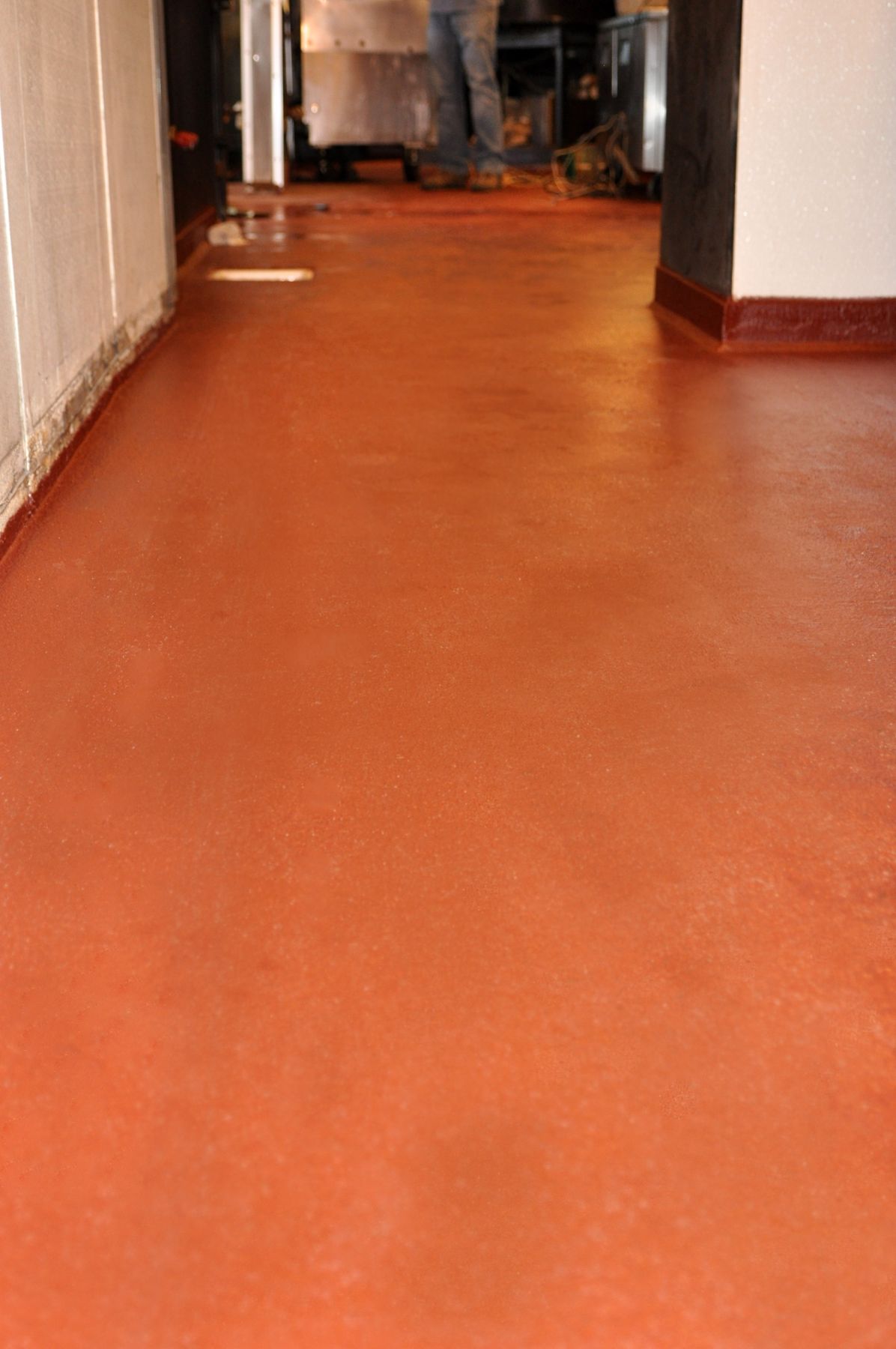 Terracotta orange seamless floor with coved base running down a restaurant kitchen corridor, portrait view