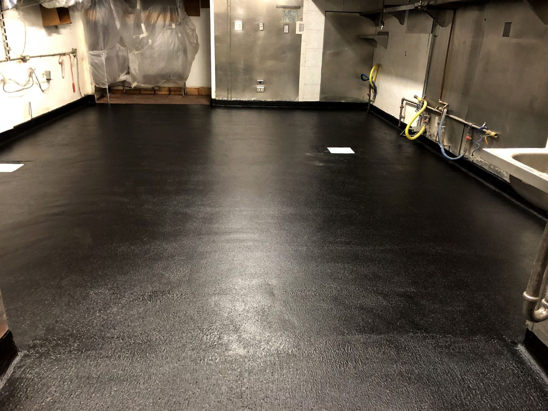 Black textured waterproof epoxy floor coating with coved edges in a commercial kitchen after installation