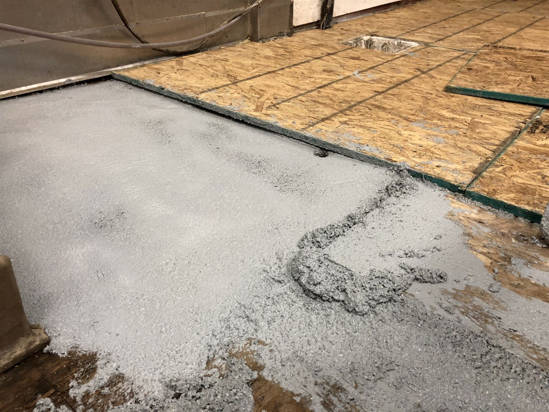Gray granular waterproofing coating being applied over rough plywood subfloor panels during floor preparation