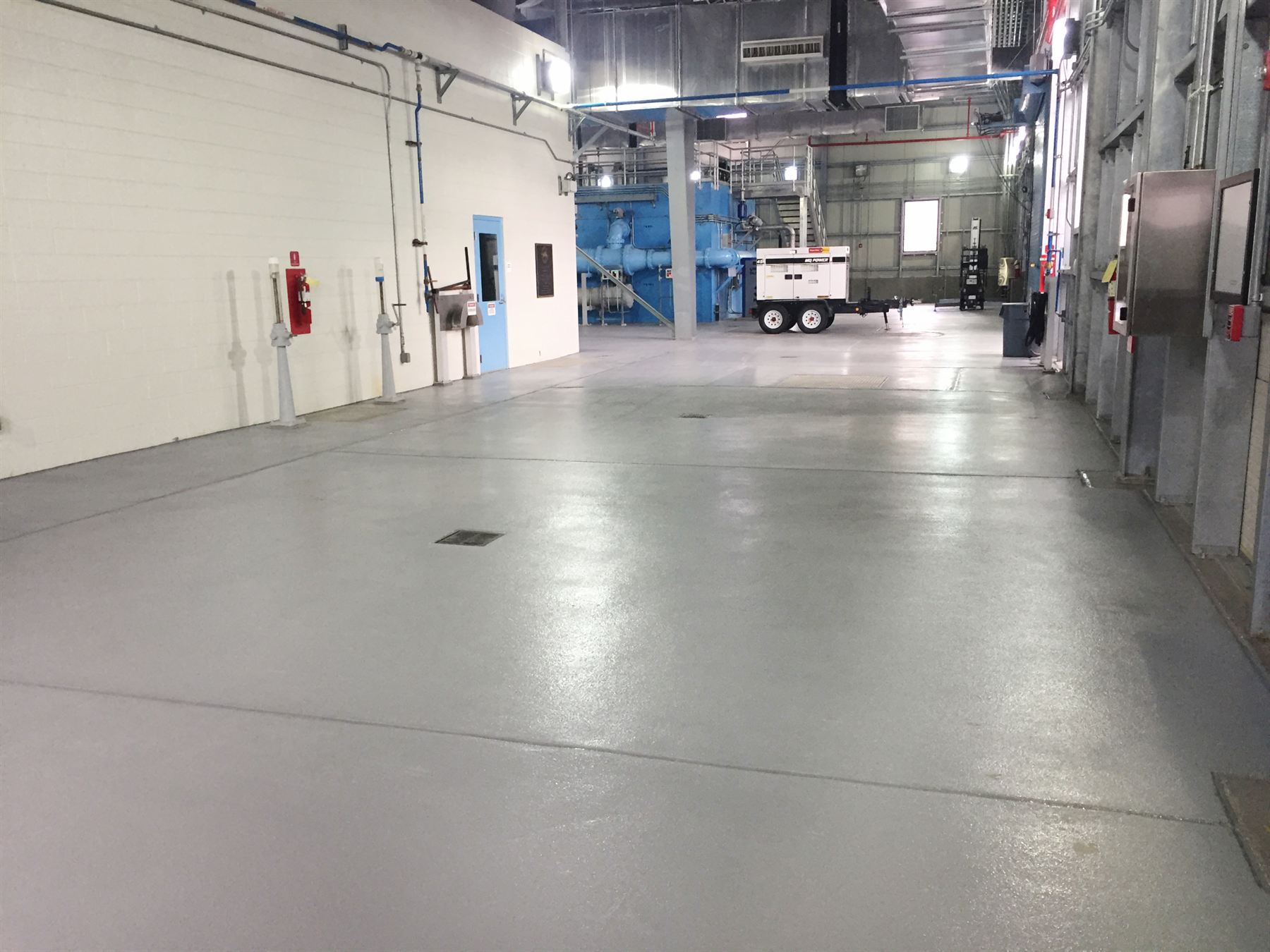 Light gray waterproof-coated concrete floor stretching through a large industrial plant with blue pumps