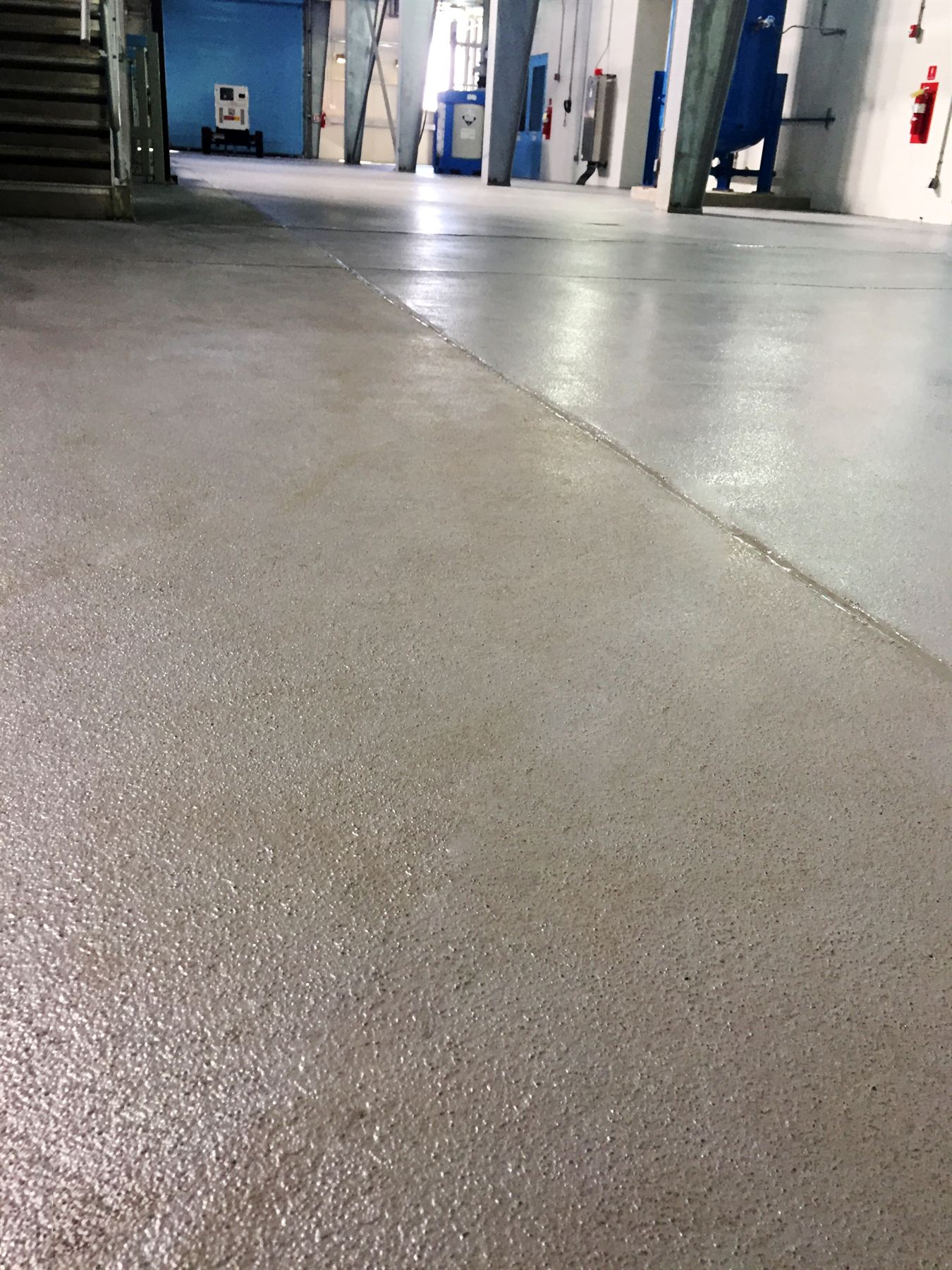 Low angle of textured beige waterproof coating meeting a glossy gray coated floor at a sealed joint